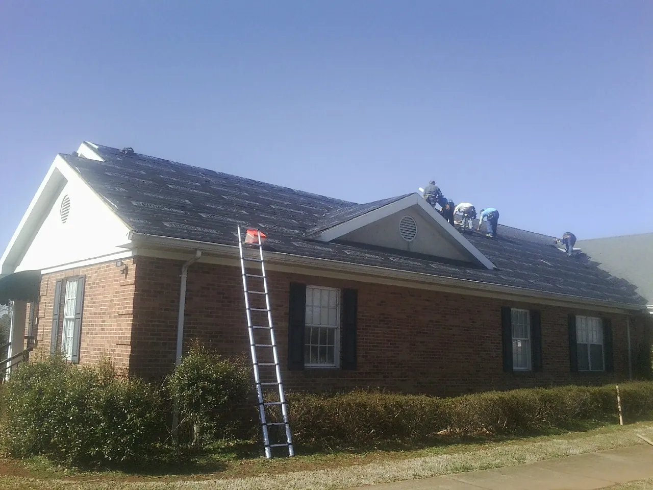 Crew tearing shingles off a brick ranch roof with a ladder set — Metal Roof Repair work by our crew in Shawnee
