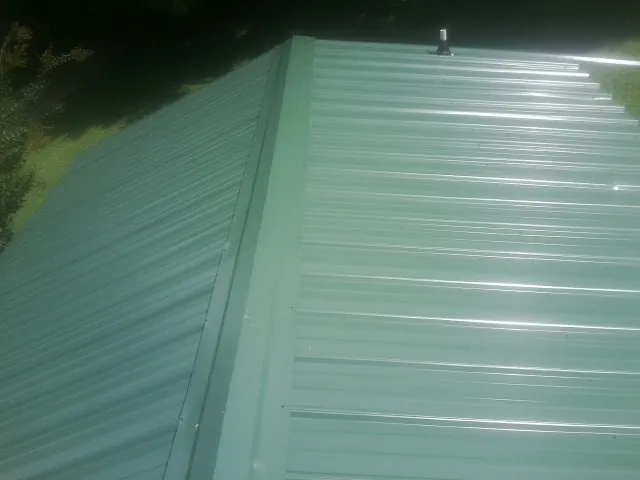 New green metal panels meeting at the ridge of a roof — Flat Roof Repair work by our crew in Shawnee